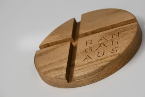 Made of solid chestnut wood. Minimalist line with clean geometric shapes. Round smartphone or tablet base made of natural wood with two vertically intersecting recesses.