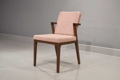 Diagonal view of dining chair Calma without arms, featuring a dark brown painted finish and pink fabric upholstery