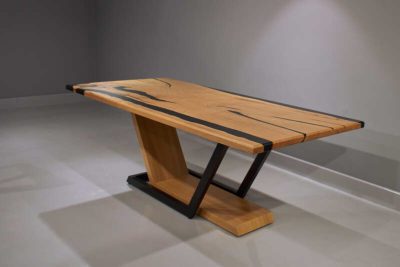 Diagonal View. Dining Table Mystique made of natural solid chestnut wood and black epoxy resin in matte finish. Geometrical central base of chestnut wood and black metal structure.
